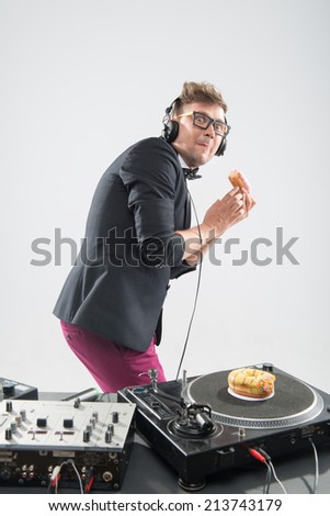 Half length portrait of DJ eating donut hiding from behind and placing donut on turntable, stylish look in tuxedo isolated on white, concept of food at work, experiment