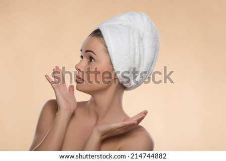 Portrait of surprised  girl in spa with clean and  fresh skin, confused looking aside and moving her hands, with a towel on her head , isolated on beige background