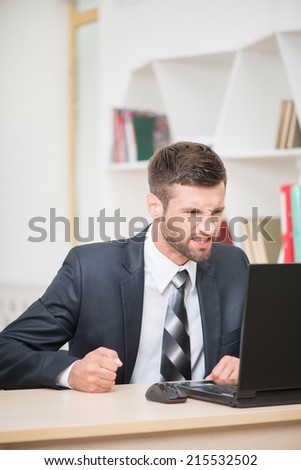 Portrait of angry businessman sitting at the table with laptop beating his hand on the table and thinking about some problems in office background