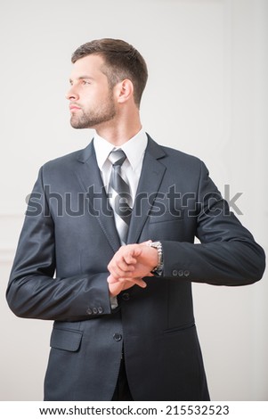 Waist-up portrait of handsome confident businessman standing and touching clock on his hand and looking aside on white background with copy place