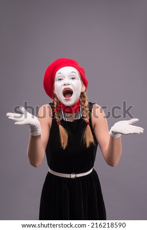 Waist-up portrait of funny female mime in red head and with white face very loudly shouting and looking at the camera isolated on grey background with copy place