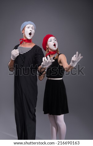 Full-length portrait of funny mime couple with white faces solemnly singing and waving their hands isolated on grey background with copy place