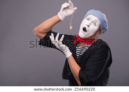 Waist-up portrait of male mime with grey hat and white face funny holding a pocket clock in his hand isolated on grey background with copy place