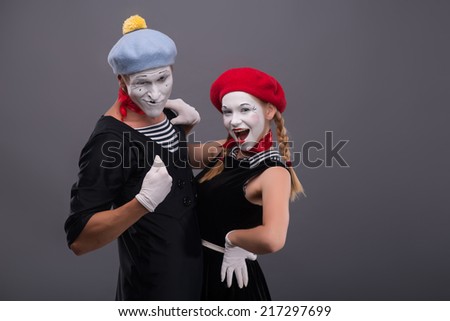 Waist-up portrait of funny hugging mime couple saucy looking at the camera, male mime showing on himself isolated on grey background with copy place