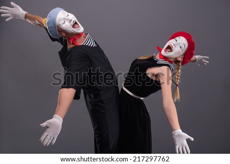 Full-length portrait of mime couple wanting to hug each other, female mime looking at the camera, male mime laughing and looking at his girlfriend isolated on grey background with copy place