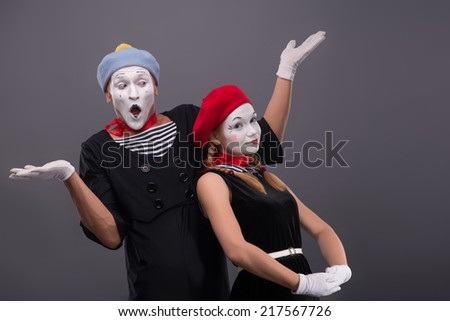 Waist-up portrait of funny mime couple, male mime breeding his hands and confused looking at his girlfriend, who is calmly looking at the camera isolated on grey background with copy place