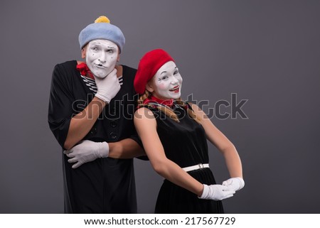 Waist-up portrait of funny mime couple, male mime scheming something, female mime looking at the camera with pretty smile isolated on grey background with copy place