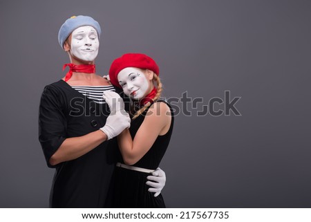Waist-up portrait of mime couple hugging with love each other isolated on grey background with copy place, male mime looking at his girlfriend, she is calmly looking at the camera