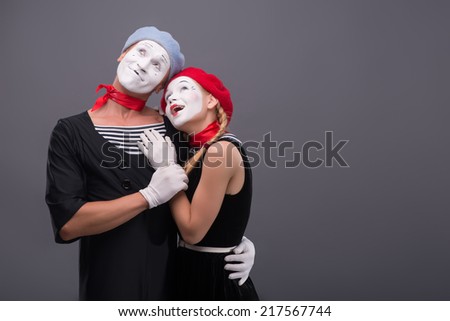 Waist-up portrait of mime couple hugging with love each other isolated on grey background with copy place, looking aside together and pretty smiling