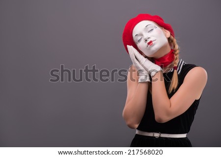 Waist-up portrait of young mime girl closing her eyes and showing with her hands that she wants to sleep isolated on grey background with copy place