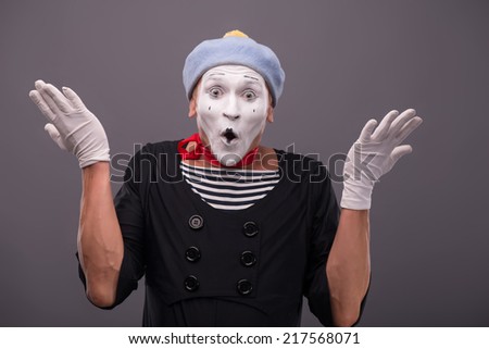 Waist-up Portrait of young mime breeding his hands and very surprised looking at the camera isolated on grey background with copy place