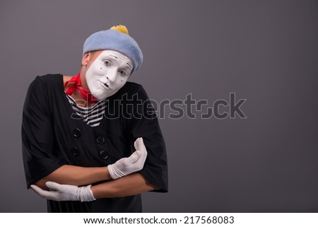 Waist-up Portrait of young mime imagining that he is holding a baby on his hands and lulling it, looking at the camera isolated on grey background with copy place