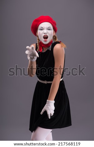 Full-length portrait of young mime girl with white face, red hat and red scarf sexy looking at the camera and showing cats gestures isolated on grey background with copy place