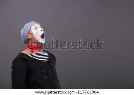 Waist-up Portrait of young male mime with white face, grey hat loudly shouting and scared looking up isolated on grey background with copy place