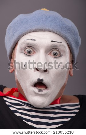 Close-up Portrait of scared young male mime with white face, grey hat opening his mouth and afraid looking at the camera isolated on grey background with copy place