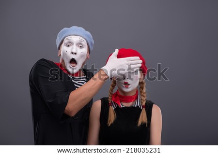 Waist-up portrait of scared mime couple, male mime looking at the camera with consternation on his face and closing eyes of his girlfriend isolated on grey background with copy place