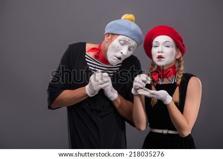 Waist-up portrait of sad mime couple pitifully crying, female mime looking at the camera and putting her tears in her hands showing them her boyfriend isolated on grey background with copy place