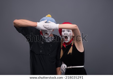 Waist-up portrait of scared mime couple, female mime looking at the camera loudly crying and closing with her hands eyes of her boyfriend isolated on grey background with copy place