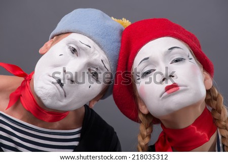 Close-up portrait of sad mime couple pitifully looking at the camera and starting to cry, isolated on grey background with copy place