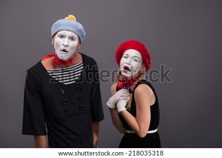 Waist-up portrait of sad mime couple pitifully crying and looking at the camera, female mime holding her hands on her chest isolated on grey background with copy place