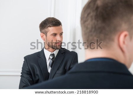 Close-up portrait of two handsome businessmen in suits in office, one businessman looking aside with selective focus on him and another standing back to the camera