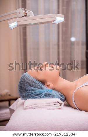 Side-view portrait of a young woman with fresh and clean skin calmly looking up and lying on a table preparing for getting a professional cosmetology procedures in healthy beauty spa salon