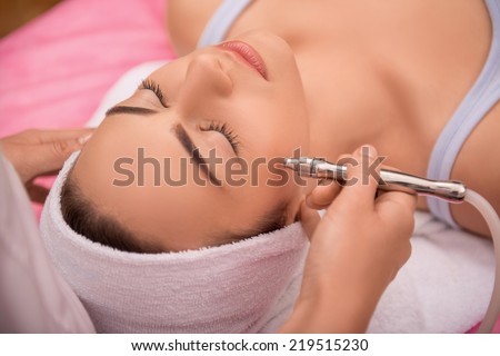 Close-up top-view side-view portrait of a young woman with a towel on her head lying on a table with closed eyes getting a laser skin treatment in healthy beauty spa salon