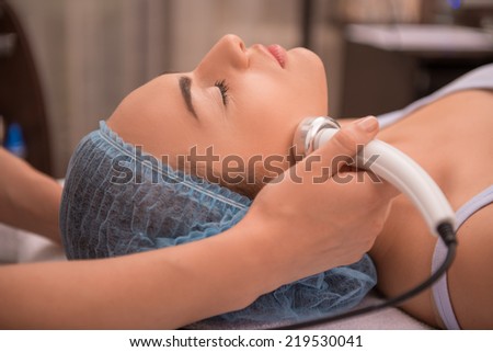 Close-up portrait of a young woman with a towel on her head lying on a table with closed eyes getting a laser skin treatment in healthy beauty spa salon