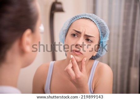 Close-up portrait of unhappy young woman looking at her doctor and showing something on her face with irritation after a professional cosmetology procedures in beauty spa salon