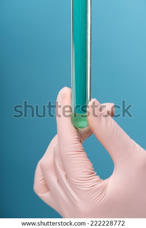 Close-up portrait of female scientist in overall holding in her hands four tubes with some substances in laboratory doing some experiments isolated on blue background, with selective focus on a tubes