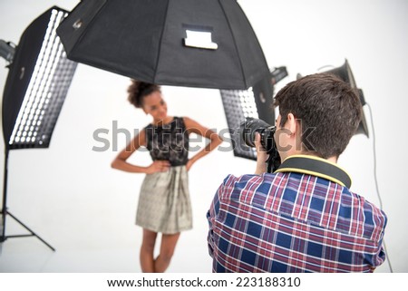 Selective focus on the photographer wearing nice checked shirt standing back to us animated his work photographing the model on background