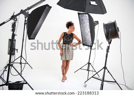 Full-length portrait of lovely African model wearing wonderful evening dress standing in front of projectors looking at someone