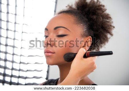 Half-length portrait of lovely African model standing in the studio with closed eyes waiting until her make-up will be ready