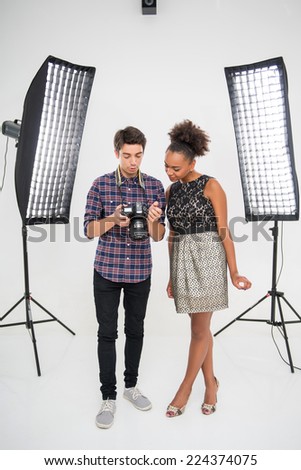 Full- length portrait of young handsome photographer wearing checked shirt standing between the projectors with the young African model showing her photos