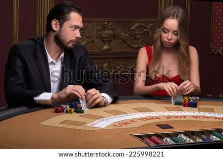 Handsome  man and beautiful woman in casino competing  holding in hands chips and cards sitting at table