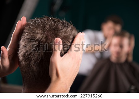 hairdresser  checks   length of  hair in mirror of handsome satisfied  client in  professional  hairdressing salon