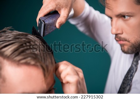 hairdresser  cuts    hair  with hair clipper on back of the head of handsome satisfied  client in  professional  hairdressing salon top view