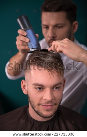 hairdresser  cuts    hair  with hair clipper on back of the head of handsome satisfied  client in  professional  hairdressing salon