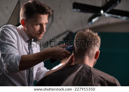hairdresser  cuts    hair  with hair clipper on back of the head of handsome satisfied  client in  professional  hairdressing salon low angle