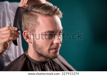 hairdresser  does   hair  with black comb of handsome satisfied  client in  professional  hairdressing salon