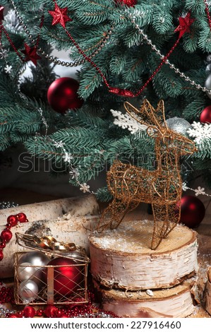 Christmas tree toys  like wicker iron gold  deer  statuette  on wooden logs   with  snowflakes near  fir with selective focus