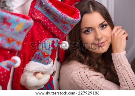 Beautiful attractive brown haired girl sitting near red Christmas socks for presents  dressed in beige knitted jacket