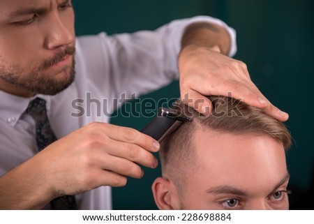 hairdresser  cuts   hair  with hair clipper  on crown of handsome satisfied  client  in  professional  hairdressing salon
