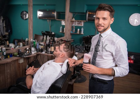 hairdresser  with brush and   handsome satisfied  client  with short haircut in  professional  hairdressing salon