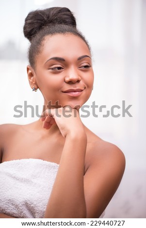 Portrait of beautiful    dark skinned girl in white towel with black curly hair in bun smiling looking down  isolated on white background