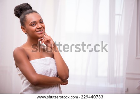 Portrait of beautiful  dark skinned girl with in white towel  in bun smiling  and touching her face  looking at camera isolated on white background  with copy place