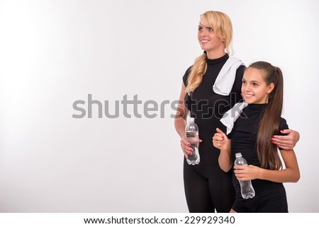 Young sport  mother with rubber mat for yoga  and her  daughter teenager with bottle  clear mineral water  and towel isolated on white background with copy place