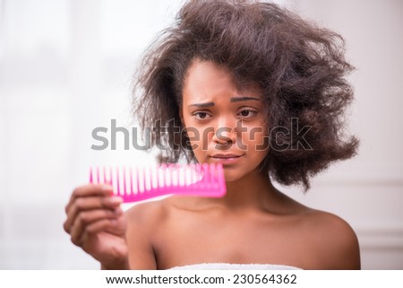 Beautiful  sad disappointed dark skinned girl being not able to  comb her hair looking at rose comb  pulling her face with tangled disorder hair isolated on white background selective focus