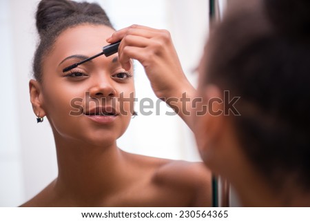 Beautiful  dark skinned girl in white towel putting  mascara on and  looking at mirror smiling  isolated on white background selective focus