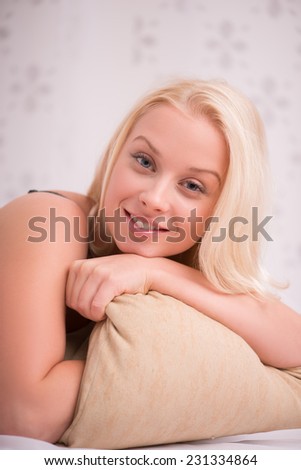 Sexy beautiful blond girl in black underclothes with blue eyes smiling  lying  beige pillow looking at  camera